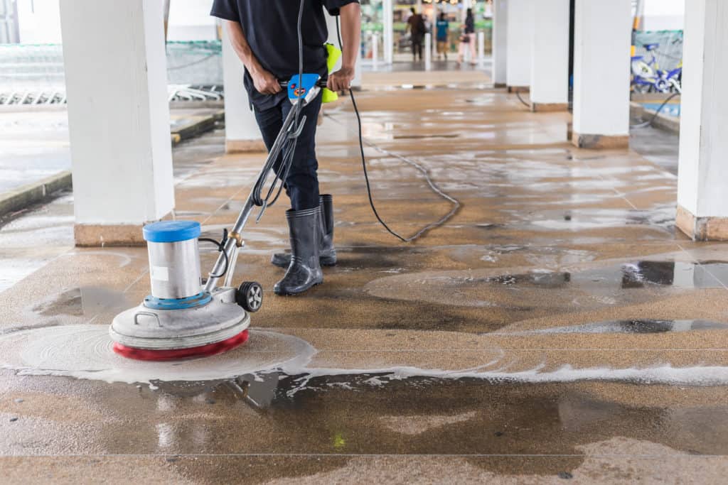Eine Reinigungskraft reinigt den Boden mit einer Einscheibenmaschine und chemischen Reinigungsmitteln