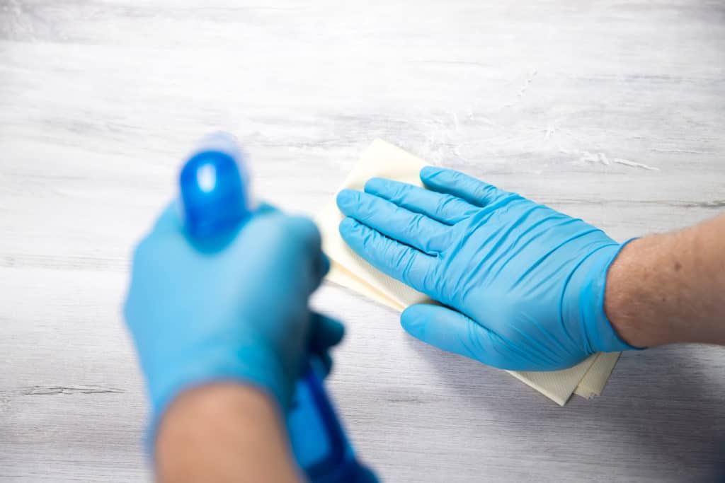 Hände überzogen mit Latexhandschuhen reinigen einen Tisch